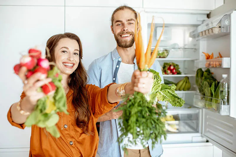 A couple happily standing with a selection of fresh vegetables, showcasing joy in a healthy lifestyle